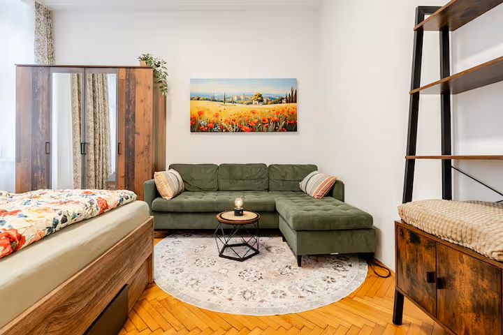 Heller Wohn- und Schlafbereich mit grünem Sofa, Bett und Parkett